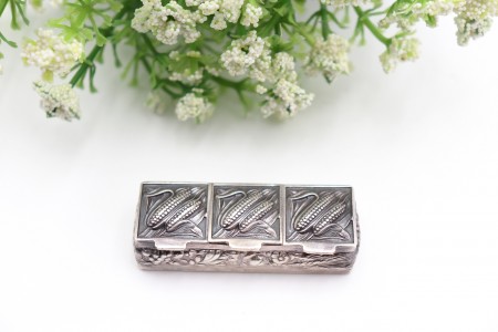 Caixa de comprimidos em prata com três divisórias e maçarocas de milho 